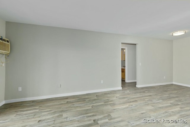 spare room featuring light wood-type flooring, baseboards, and an AC wall unit