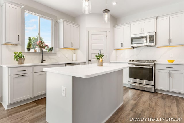 kitchen featuring stainless steel appliances, light countertops, a kitchen island, a sink, and wood finished floors