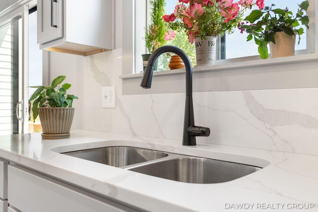 room details featuring tasteful backsplash, white cabinetry, a sink, and light stone countertops