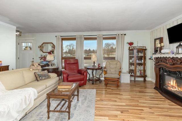 living room featuring light wood finished floors, plenty of natural light, ornamental molding, and a glass covered fireplace