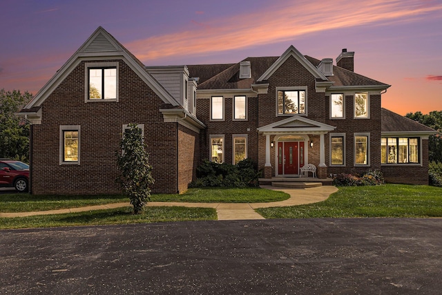 view of front facade with brick siding, a front lawn, and a chimney