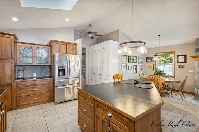 kitchen featuring dark countertops, vaulted ceiling with skylight, brown cabinets, and stainless steel fridge with ice dispenser