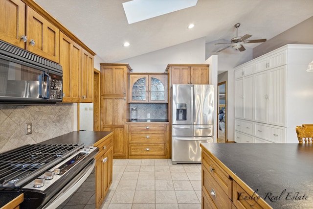 kitchen featuring brown cabinets, stainless steel appliances, dark countertops, tasteful backsplash, and vaulted ceiling with skylight