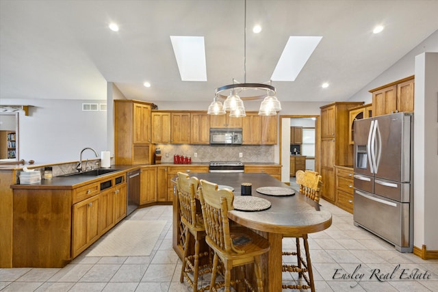 kitchen with brown cabinets, stainless steel appliances, backsplash, a sink, and vaulted ceiling with skylight