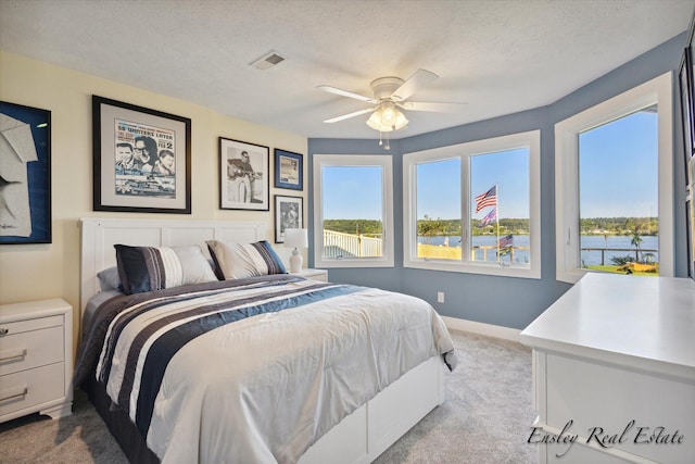 carpeted bedroom featuring a textured ceiling, multiple windows, visible vents, and baseboards