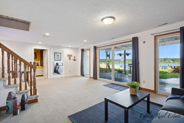 living area with visible vents, light carpet, a textured ceiling, baseboards, and stairs