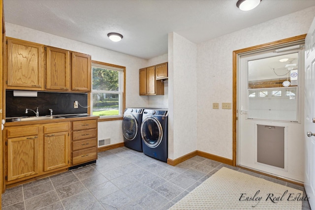 clothes washing area with cabinet space, baseboards, visible vents, washing machine and clothes dryer, and a sink