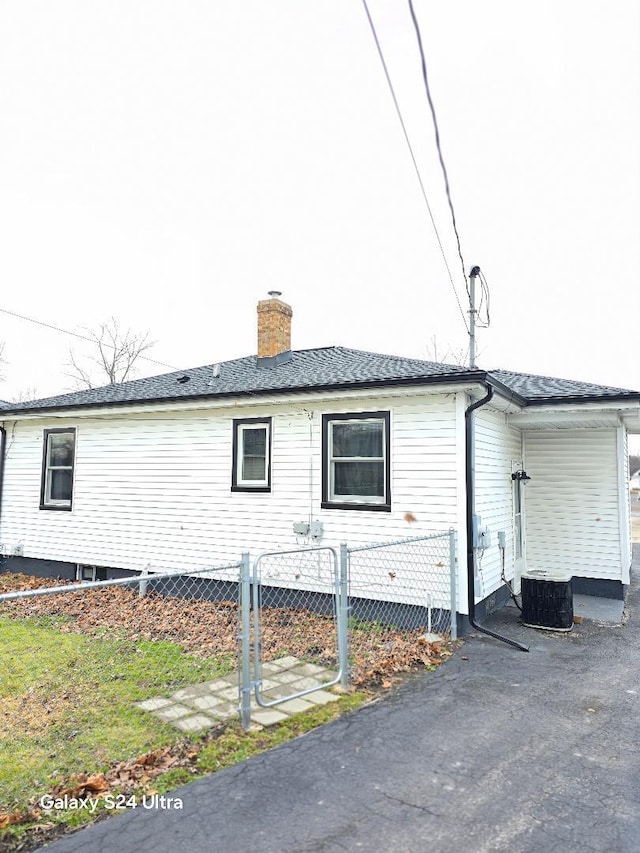 view of side of home with a chimney, fence, and cooling unit