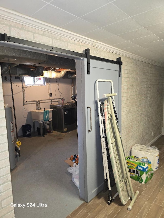 below grade area with a barn door, brick wall, a sink, water heater, and crown molding