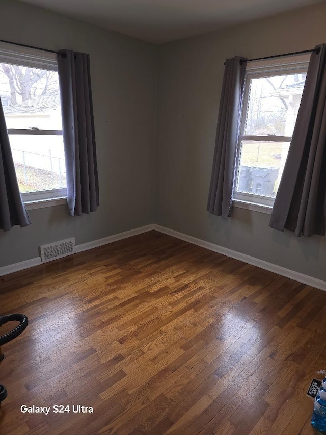 empty room with hardwood / wood-style flooring, baseboards, and visible vents