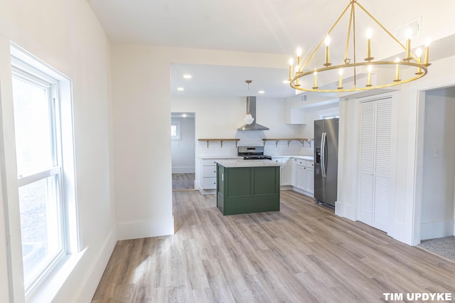 kitchen with light countertops, appliances with stainless steel finishes, a kitchen island, wall chimney range hood, and light wood-type flooring