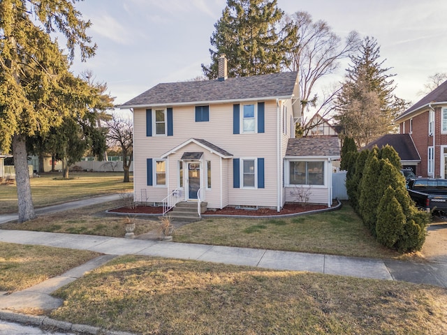 colonial inspired home featuring a shingled roof, a front yard, and a chimney