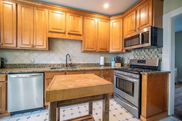 kitchen with stainless steel appliances, dark stone countertops, a sink, and light floors