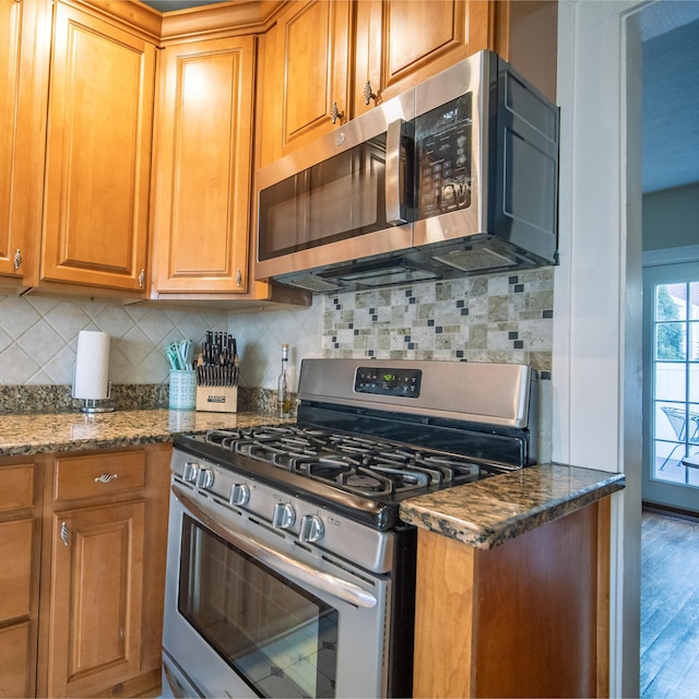 kitchen featuring dark stone countertops, stainless steel appliances, backsplash, and wood finished floors