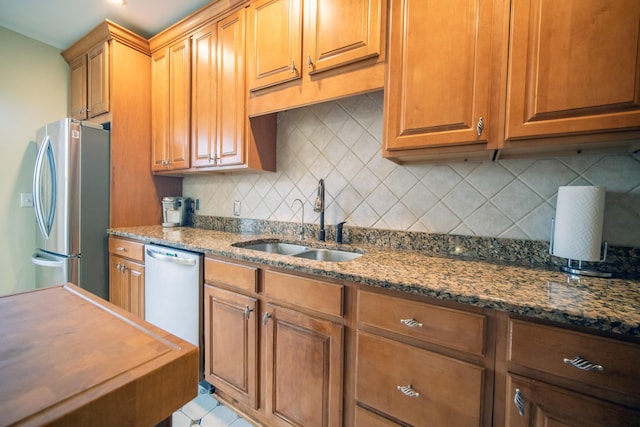 kitchen with a sink, appliances with stainless steel finishes, dark stone counters, tasteful backsplash, and brown cabinetry