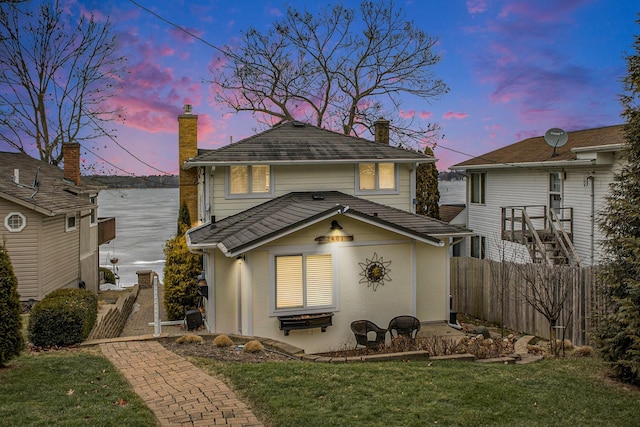 back of property at dusk with a yard, a chimney, fence, and stucco siding