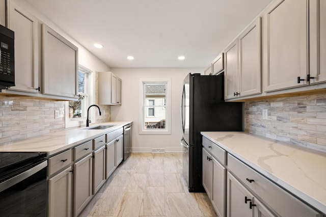 kitchen featuring light stone counters, recessed lighting, a sink, black appliances, and baseboards