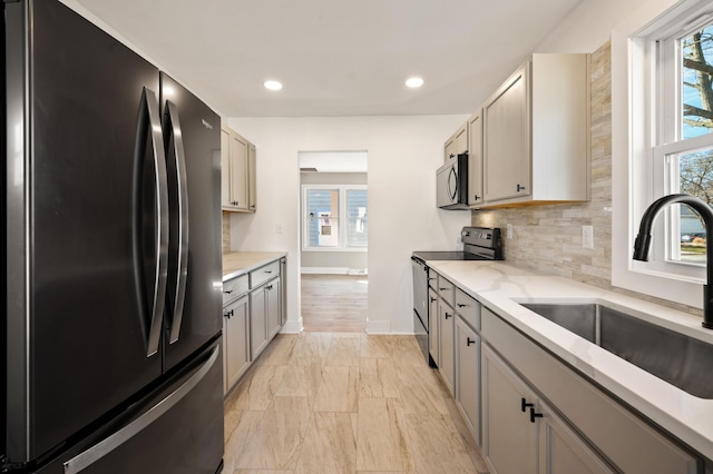 kitchen with stainless steel appliances, a wealth of natural light, a sink, and light stone countertops