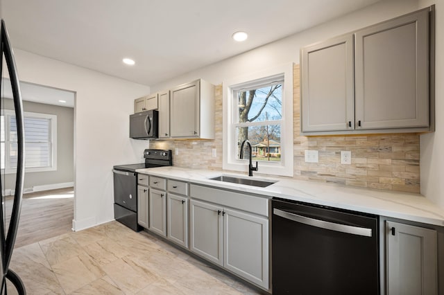 kitchen with light stone countertops, black appliances, gray cabinets, and a sink