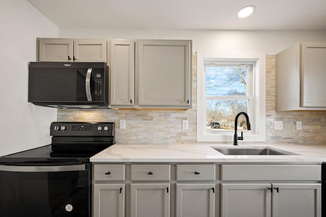 kitchen featuring light stone counters, recessed lighting, a sink, decorative backsplash, and black appliances