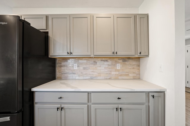 kitchen with light stone counters, freestanding refrigerator, and backsplash