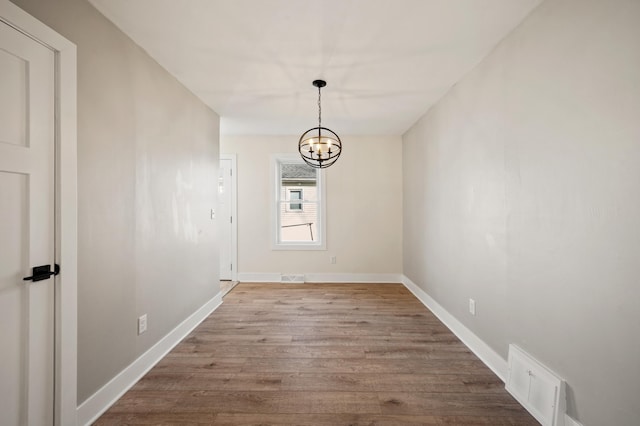 unfurnished dining area featuring a chandelier, wood finished floors, visible vents, and baseboards