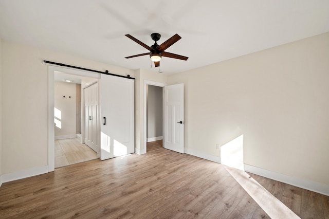 unfurnished bedroom with a barn door, baseboards, connected bathroom, ceiling fan, and wood finished floors