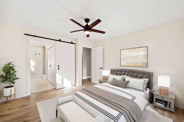 bedroom featuring a barn door, baseboards, ceiling fan, wood finished floors, and ensuite bathroom