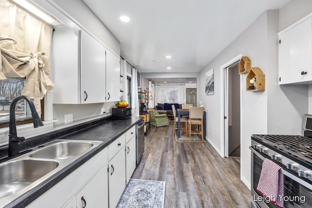 kitchen featuring dark countertops, appliances with stainless steel finishes, wood finished floors, white cabinets, and a sink