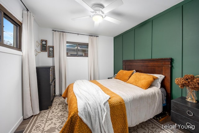 bedroom featuring wood finished floors, multiple windows, ceiling fan, and a decorative wall