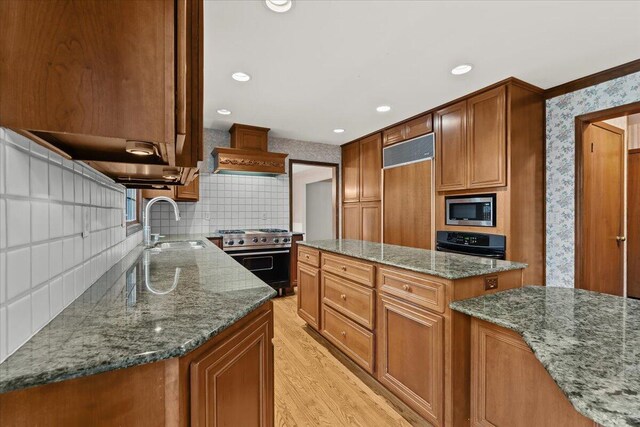 kitchen with light wood finished floors, custom range hood, built in appliances, stone counters, and a sink