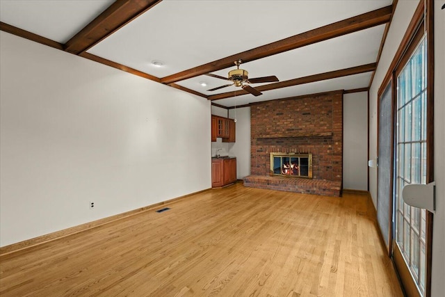unfurnished living room featuring light wood finished floors, a ceiling fan, a brick fireplace, beamed ceiling, and baseboards