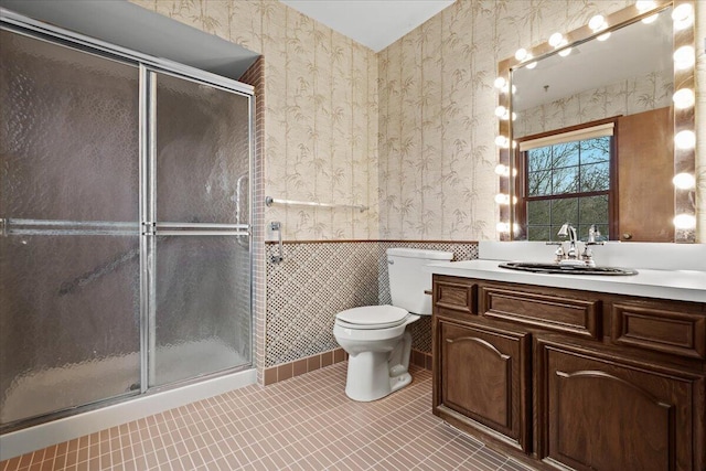 full bathroom featuring a wainscoted wall, toilet, vanity, a shower stall, and wallpapered walls