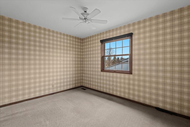 carpeted spare room with wallpapered walls, visible vents, baseboards, and ceiling fan