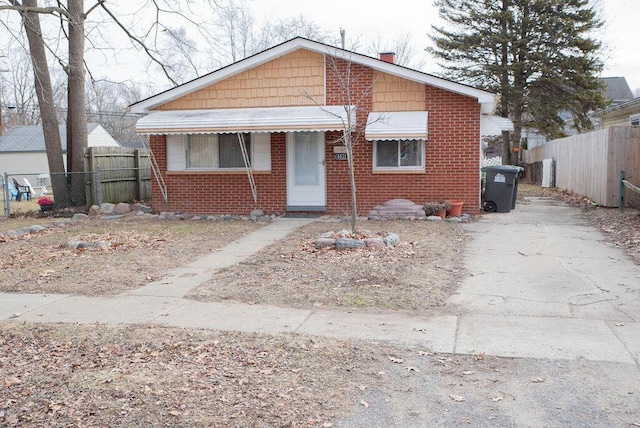 bungalow with brick siding, a chimney, and fence