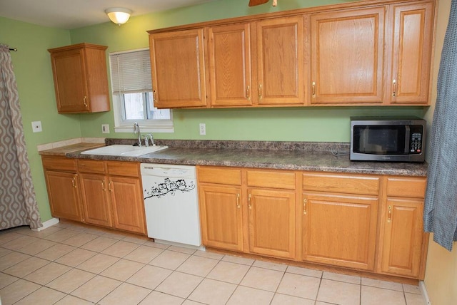 kitchen with light tile patterned floors, dark countertops, stainless steel microwave, a sink, and dishwasher