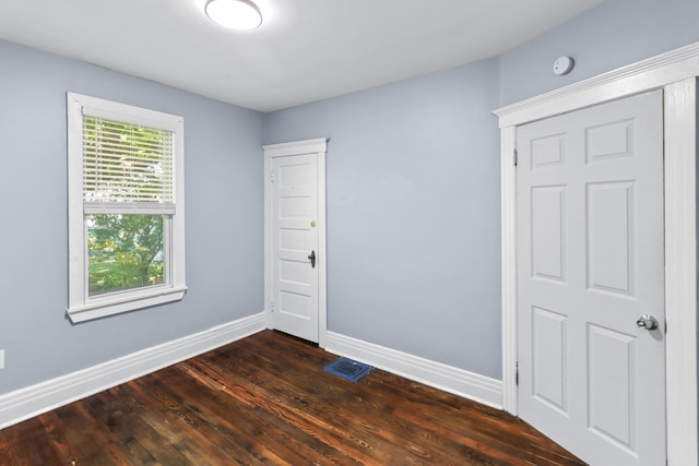 unfurnished room featuring dark wood-type flooring, visible vents, and baseboards