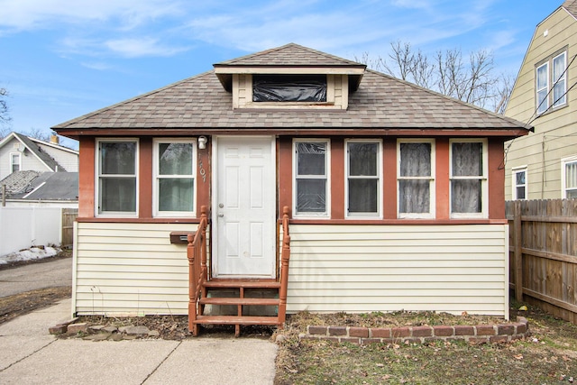 back of property with entry steps, a shingled roof, and fence