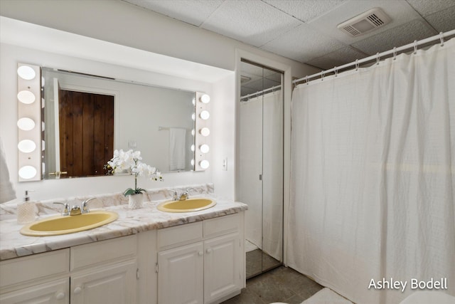 bathroom with a paneled ceiling, visible vents, a sink, and double vanity