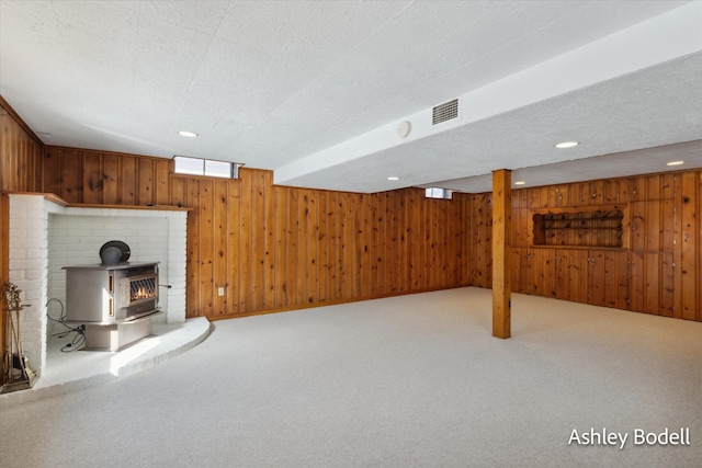 basement featuring carpet floors, wood walls, and a wood stove