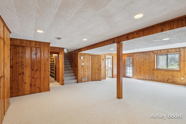 below grade area featuring a textured ceiling, carpet floors, wood walls, visible vents, and stairs