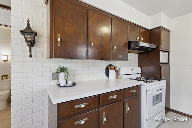 kitchen featuring tasteful backsplash, light countertops, dark brown cabinets, white appliances, and under cabinet range hood