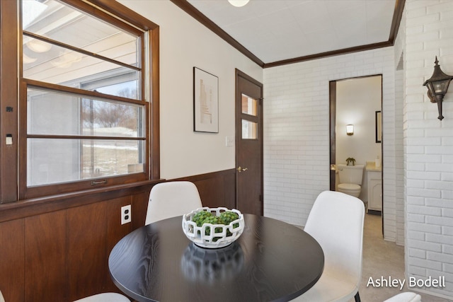 dining space featuring brick wall, ornamental molding, and wainscoting