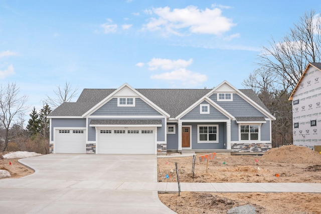 view of front of house with stone siding, concrete driveway, a shingled roof, and a garage