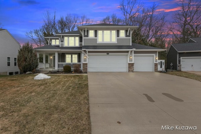 prairie-style home with a garage, concrete driveway, stone siding, covered porch, and a front yard