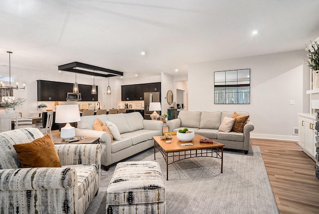 living area with baseboards, recessed lighting, an inviting chandelier, and light wood-style floors