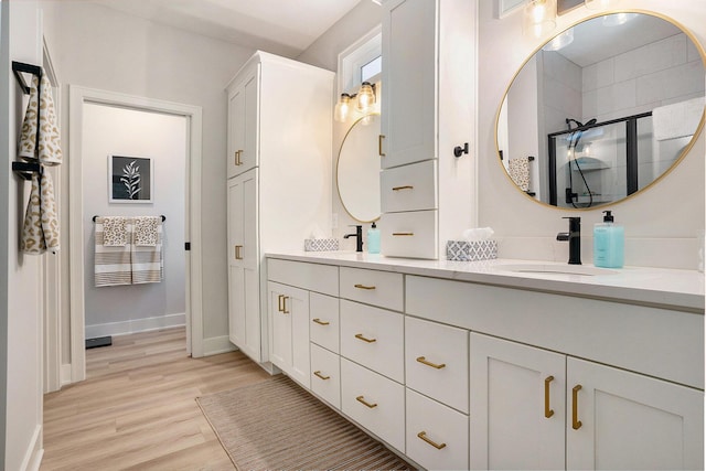full bathroom featuring a sink, wood finished floors, baseboards, a shower stall, and double vanity