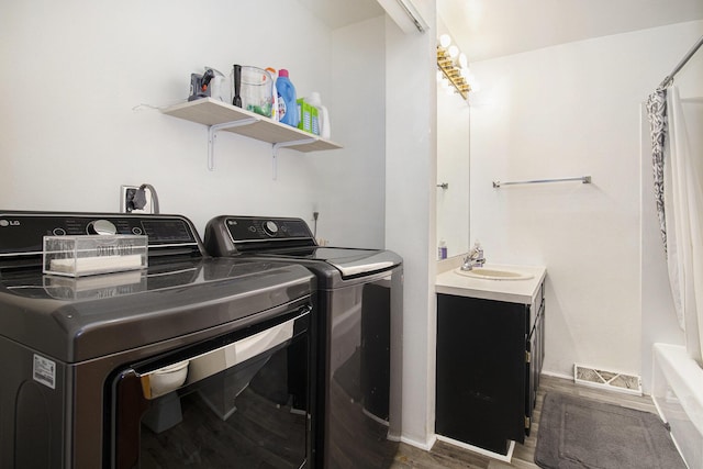 laundry room featuring visible vents, a sink, washer and clothes dryer, and wood finished floors