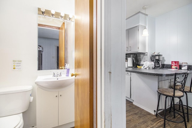 half bathroom with vanity, wood finished floors, and toilet