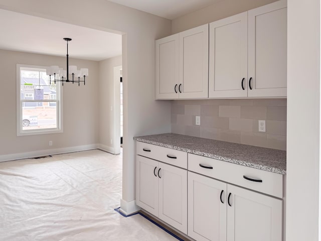 10712 Melanie Dr, Allendale, MI 49401 - kitchen featuring pendant lighting, light stone countertops, white cabinetry, tasteful backsplash, and a notable chandelier